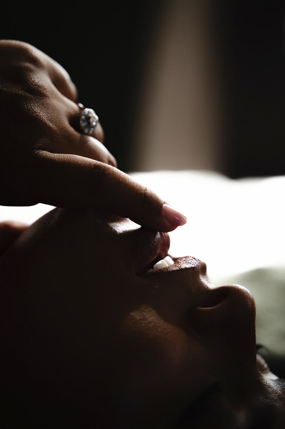 A close-up portrait of a woman’s face and hand in warm window light