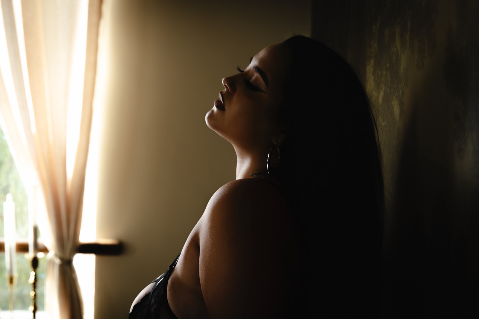 A woman in profile beside the studio window, softly lit against an olive backdrop